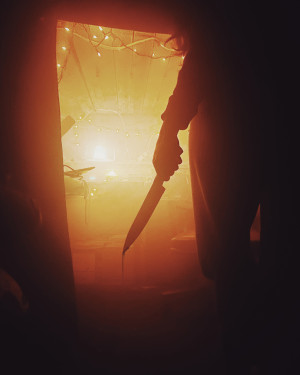 Silhouette figure standing in a doorway, holding a bloodied knife